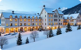 Snow-covered Beaver Creek Resort building with warm lights glowing, set against a backdrop of pine trees and distant mountains in winter.