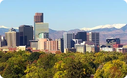 Panoramic view of the Denver skyline framed by the Rocky Mountains and lush fall foliage—capturing the vibrant contrast of urban life and natural beauty from City Park.