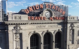 Historic Denver Union Station with its iconic "Travel by Train" neon sign and grand architecture—serving as a central hub for travel, dining, and city history in downtown Denver.