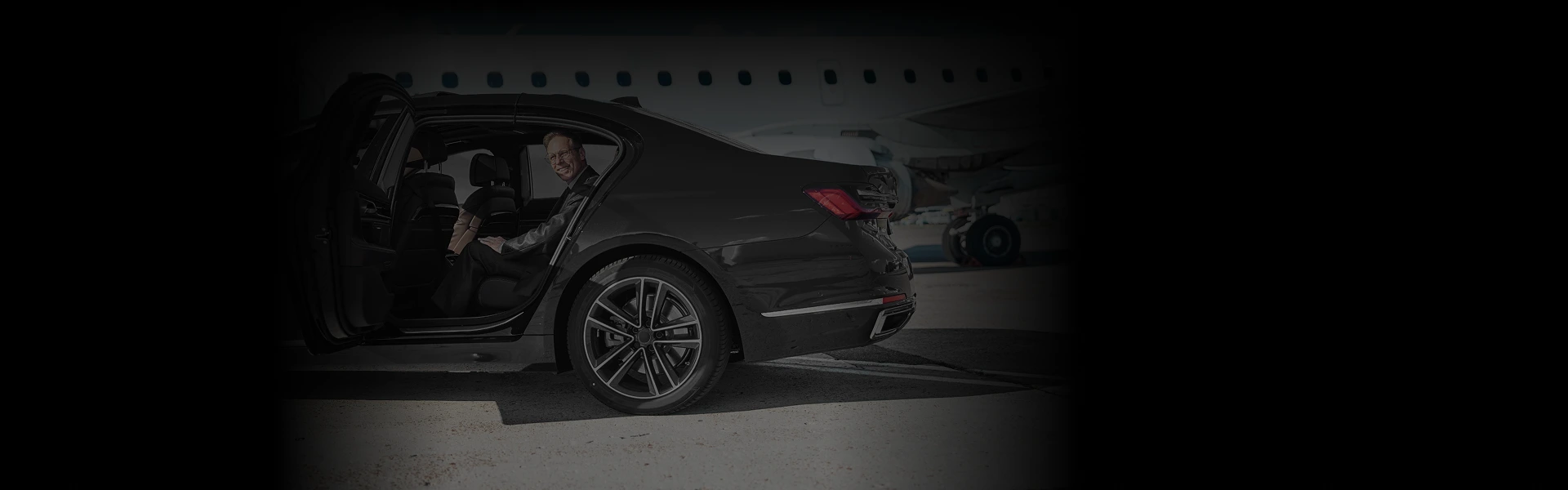 Smiling passenger steps into a luxury black sedan at an airport runway—capturing the ease, style, and professionalism of Denver Airport Car Service.